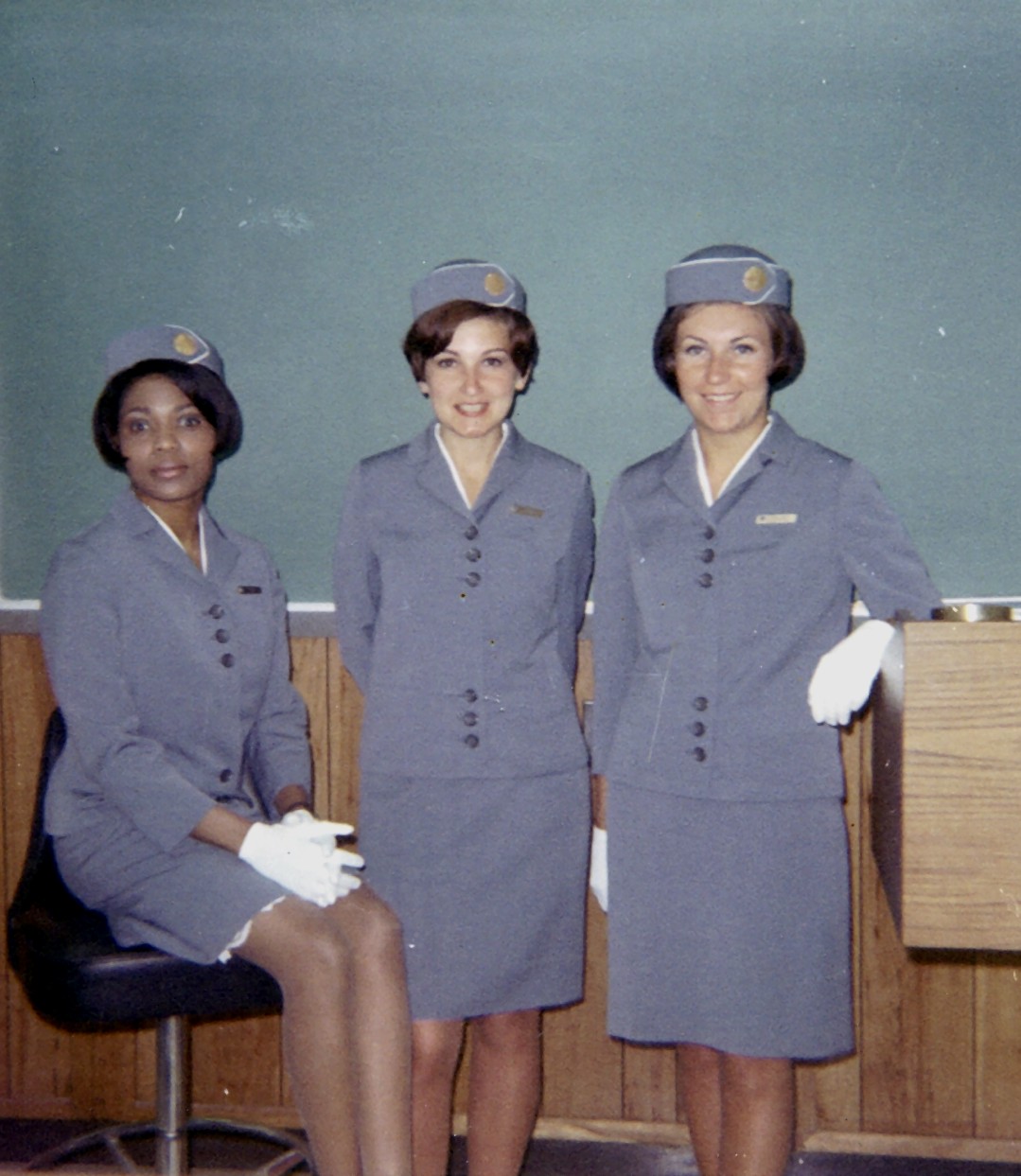 1968 April, Ouida (Judy) Stewart, Donuta (Diane) Wolk, Maureen van Leeuwen pose by the black board in a classroom at the Pan Am Flight Service Academy